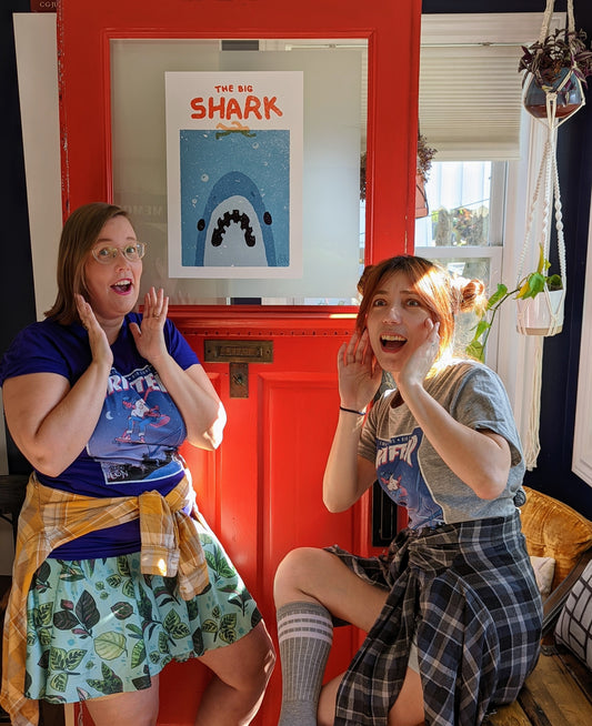 A poster stylized to parody the movie Jaws. At the top it says “THE BIG SHARK” in a cartoonish font in red. Below that is a cartoon outline of a person swimming over of an enormous Shark mouth. The shark is blue, white and black and it sits on a distressed, grainy, light blue square background. In the bottom right corner there is small blue THE BIG CON logo. The whole poster sits on a white background.