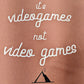 A Dusty Rose T-Shirt, with cursive writing on it in white. In lowercase letters the first line reads “it’s”, the second line “videogames” spelt as one word, the third line “not” and the fourth line “video games” using two words. In the centre below the text is the Mighty Yell logo in black which features the illustration of a mountain and a person on top yelling. There are three small lines coming out of the person’s mouth.