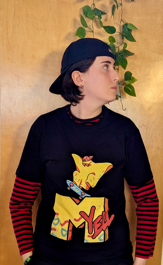 A person standing in front of a wood wall wearing a black shirt with the character Rad Ghost skateboarding over top a large "M" and the word "yell" in the style of MTV. The images are in yellow with pops of Orange, blue and pink.