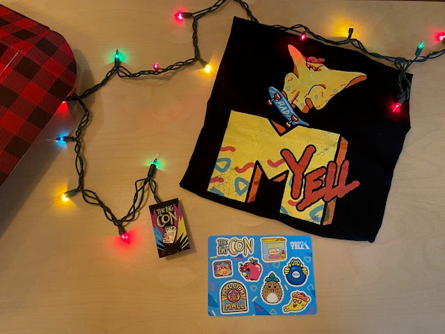 Unboxed items sit on a table. A black t-shirt featuring the character rad ghost, a hard enamel pin of the character Ali and a VHS tape. The pin is in black nickel. There is a brightly coloured sticker sheet featuring eight stickers from The Big Con. 