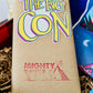 A VHS tape is covered in craft paper. There is a sticker on it of The Big Con logo that is black, white, hot pink, yellow and blue. Below that it is stamped with the Mighty Yell logo in hot pink.