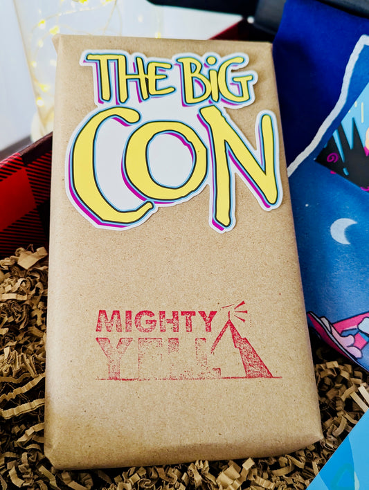 A VHS tape is covered in craft paper. There is a sticker on it of The Big Con logo that is black, white, hot pink, yellow and blue. Below that it is stamped with the Mighty Yell logo in hot pink.
