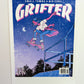 A poster that says "GRIFTER," stylized like an old THRASHER magazine cover, featuring Ali from The Big Con jumping on a skateboard over some stairs. Image stylized like a magazine cover in rectangle on the front of the shirt. Magazine cover colours are largely Blue, light blue, and pink, like a stylized night sky. The magazine cover has a distressed look, like an old print.