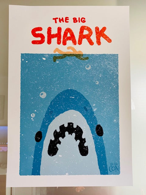 A poster stylized to parody the movie Jaws. At the top it says “THE BIG SHARK” in a cartoonish font in red. Below that is a cartoon outline of a person swimming over of an enormous Shark mouth. The shark is blue, white and black and it sits on a distressed, grainy, light blue square background. In the bottom right corner there is small blue THE BIG CON logo. The whole poster sits on a white background.