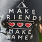 A t-shirt with the words "Make Friends Make Games," featuring 3 hearts like in a Zelda Game, and the MIghty Yell Mountain Logo, arranged aesthetically on the front of the shirt. Charcoal grey shirt with white text and red hearts.