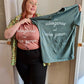A Dusty Rose T-Shirt and a Sage Green T-Shirt, both have cursive writing on it in white. In lowercase letters the first line reads “it’s”, the second line “videogames” spelt as one word, the third line “not” and the fourth line “video games” using two words. In the centre below the text is the Mighty Yell logo in black which features the illustration of a mountain and a person on top yelling. There are three small lines coming out of the person’s mouth.